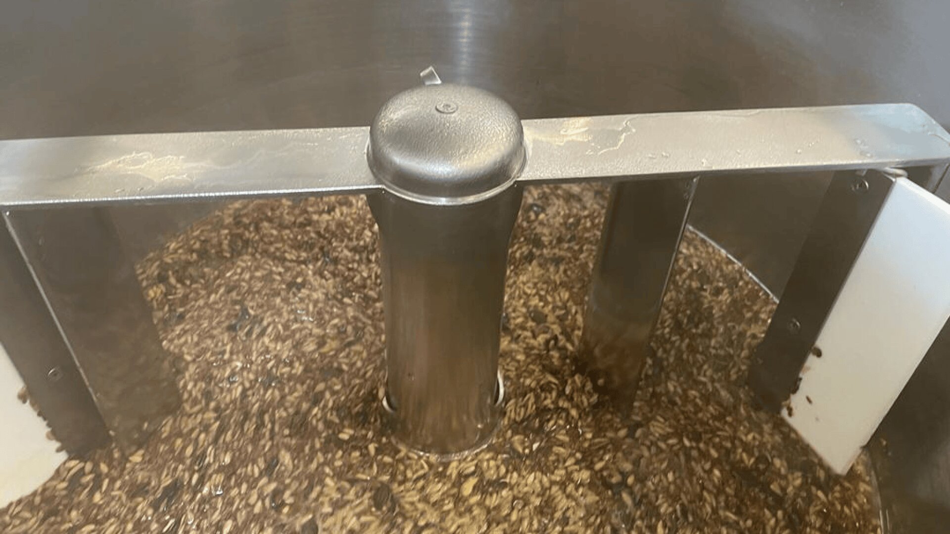 Close-up of a brewing vessel with a metal agitator stirring a mixture of grains and liquid during the mashing process in beer production.