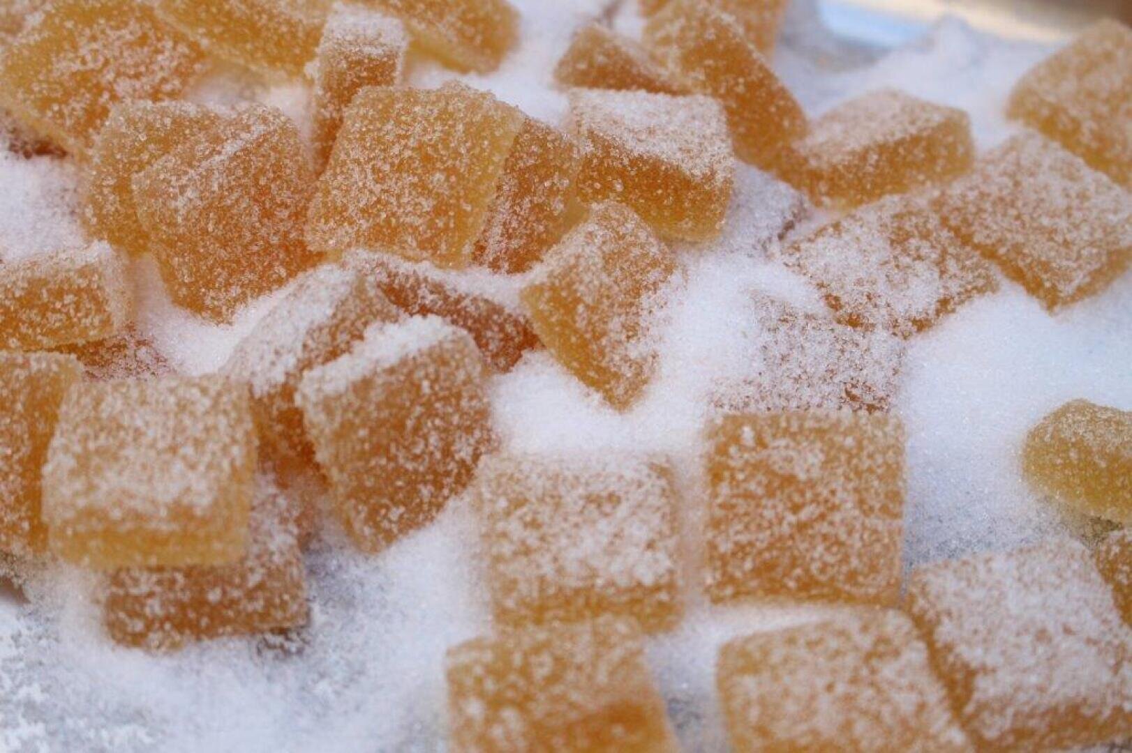 Close-up of golden-brown, sugar-coated gummy candy squares scattered on a surface covered with granulated sugar.