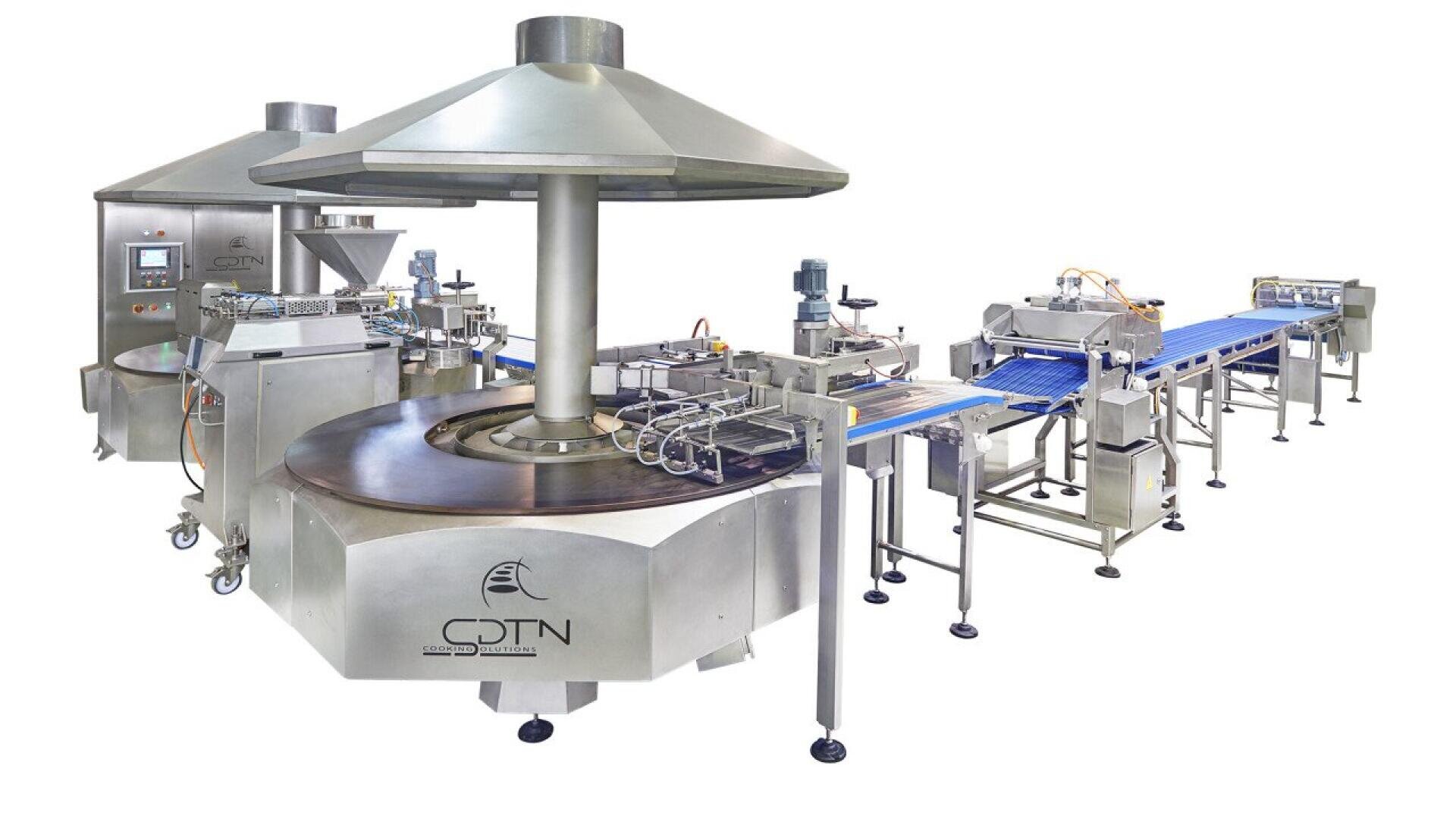 Eine große industrielle Lebensmittelverarbeitungsmaschine aus Edelstahl mit einem kreisförmigen Drehbereich, Förderbändern und automatischer Steuerung. Die Einrichtung ist sauber und modern und für die Massenproduktion in einem kommerziellen Umfeld konzipiert.