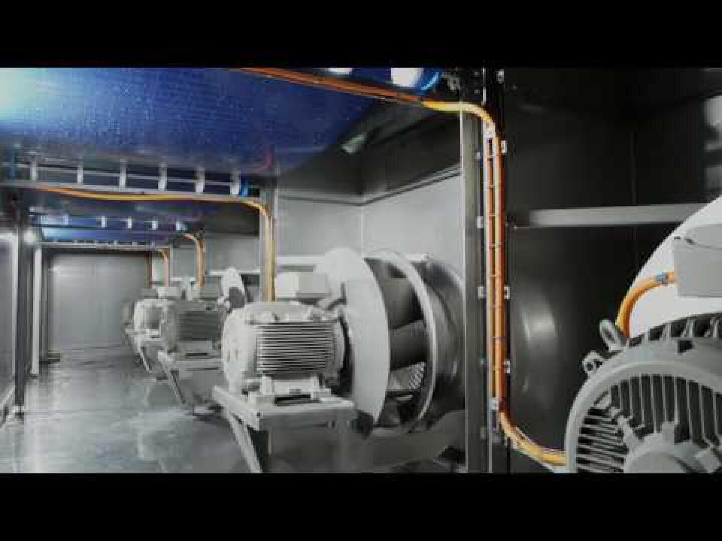 Industrial fans and motors are lined up in a large metal housing, orange power cables run along the walls and ceiling, creating a clean and organized industrial environment.