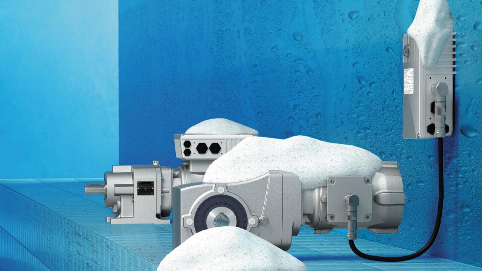 Industrial machinery coated in white foam sits on a tiled surface with a wet, blue background, suggesting a washdown or cleaning process, typically used in food or sanitary environments.
