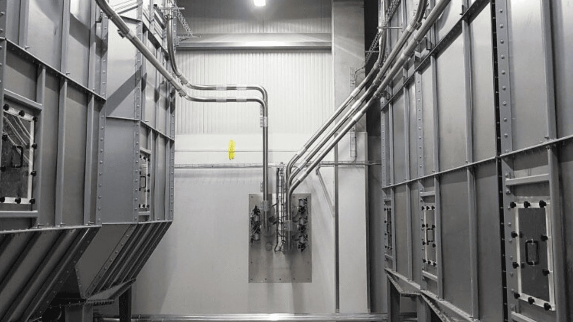Das Innere einer modernen Industrieanlage mit großen Metallplatten, Rohren und Kabeln, die an den Wänden entlanglaufen, mit Deckenbeleuchtung und einer sauberen, organisierten Umgebung.