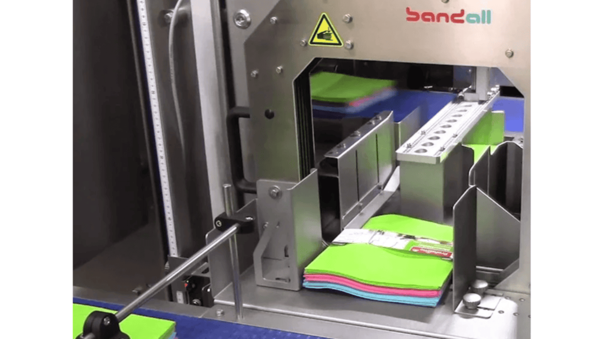 A machine labeled Bandall wraps colorful stacks of folded cloths or towels with a packaging band in an automated process.