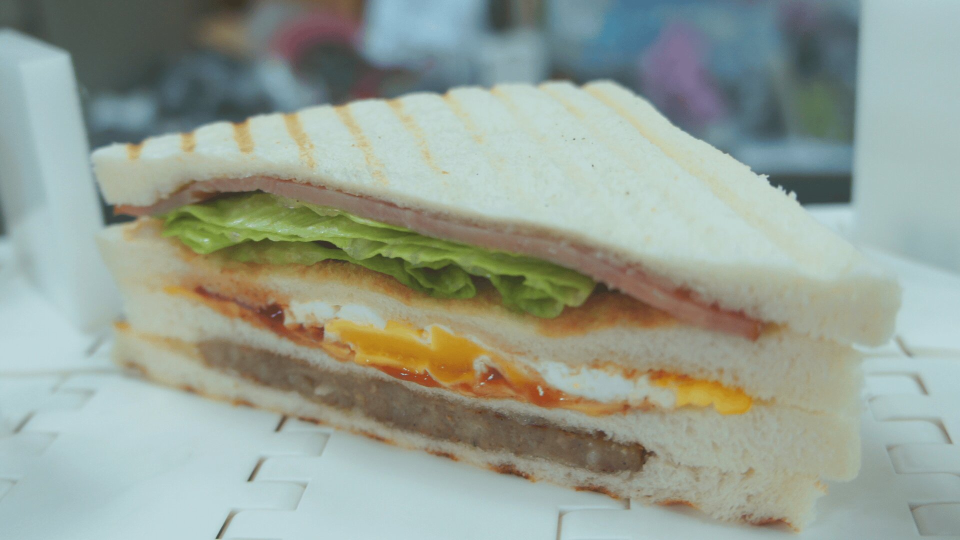 Eine Nahaufnahme einer Sandwichscheibe mit Schichten von Weißbrot, Salat, Schinken, Ei, Käse, Wurst und Gewürzen, die den Querschnitt aller Zutaten zeigt.