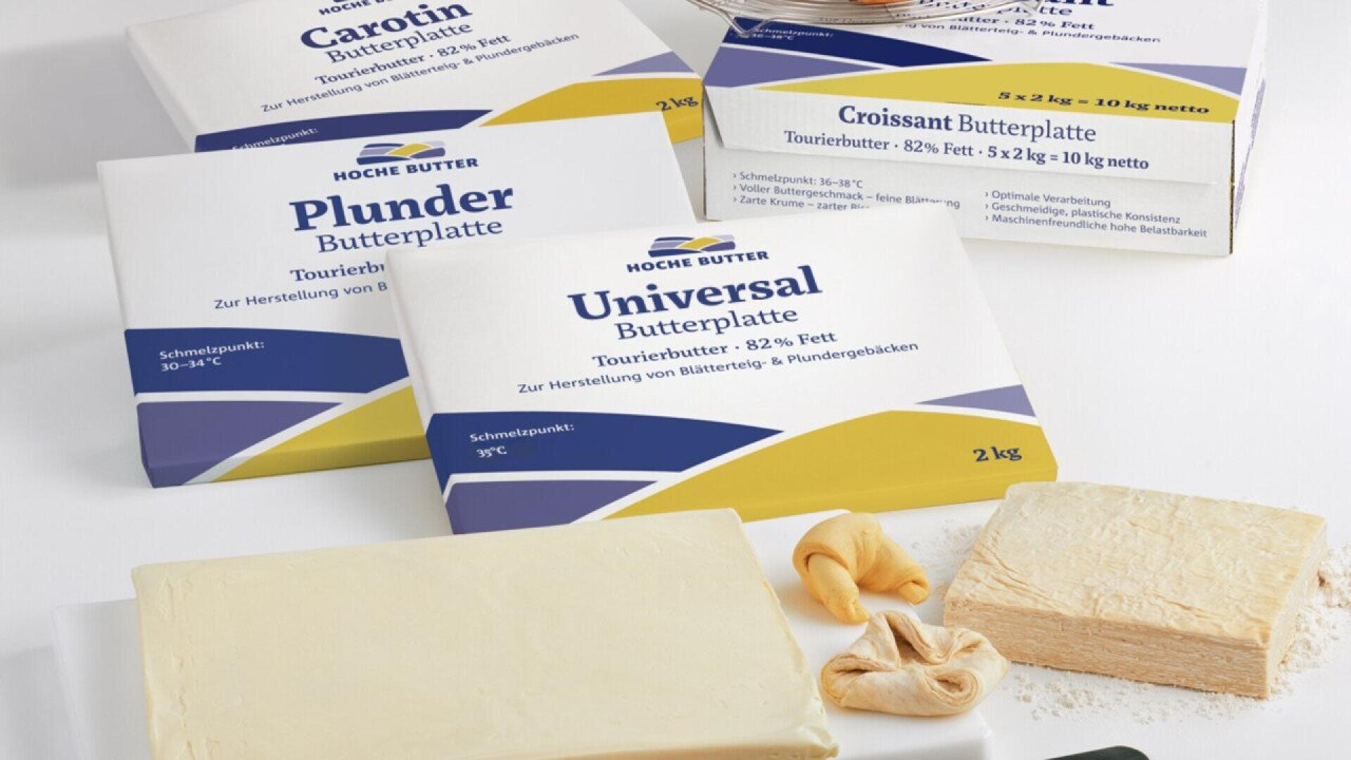Blocks of butter labeled Carotin, Plunder, and Universal Butterplatte on a white surface, with two unwrapped butter slabs and two small pieces of croissant dough in the foreground.