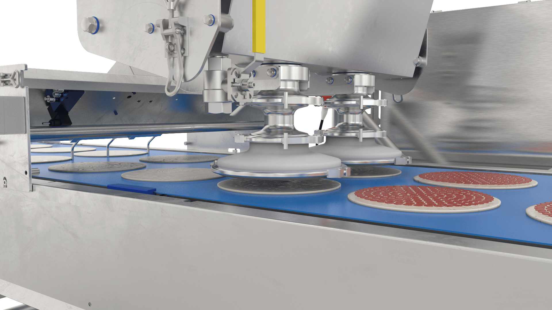 A close-up of an industrial machine placing pizza bases with sauce onto a conveyor belt in a food processing facility. The machine features multiple suction heads and stainless steel components.