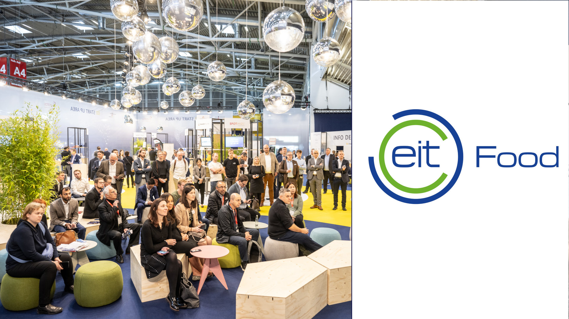 A group of people sit and stand in a modern event space with spherical hanging lights and greenery, attentively watching a presentation. The EIT Food logo is displayed on a white panel to the right.