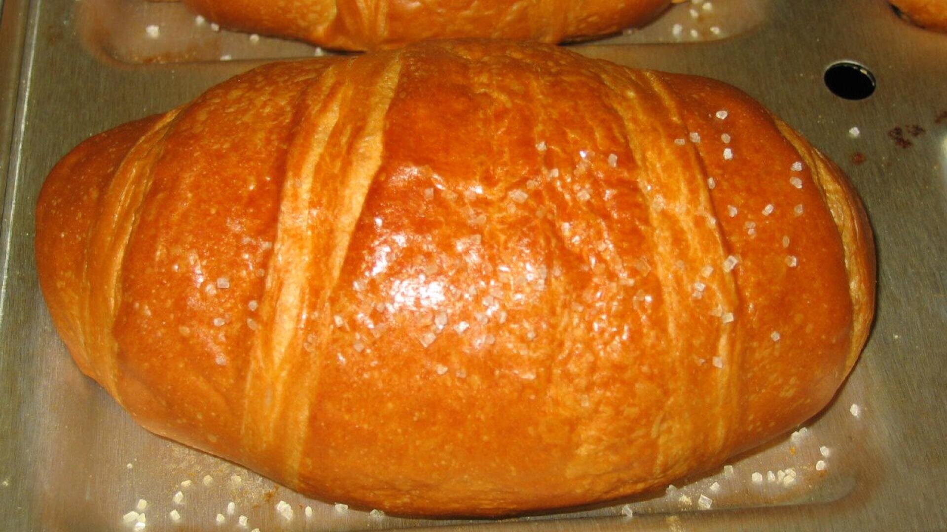 Nahaufnahme eines goldbraunen Gebäcks mit glänzender, glasierter Oberfläche und grobem Zucker auf der Oberseite, das auf einem Metallblech ruht.