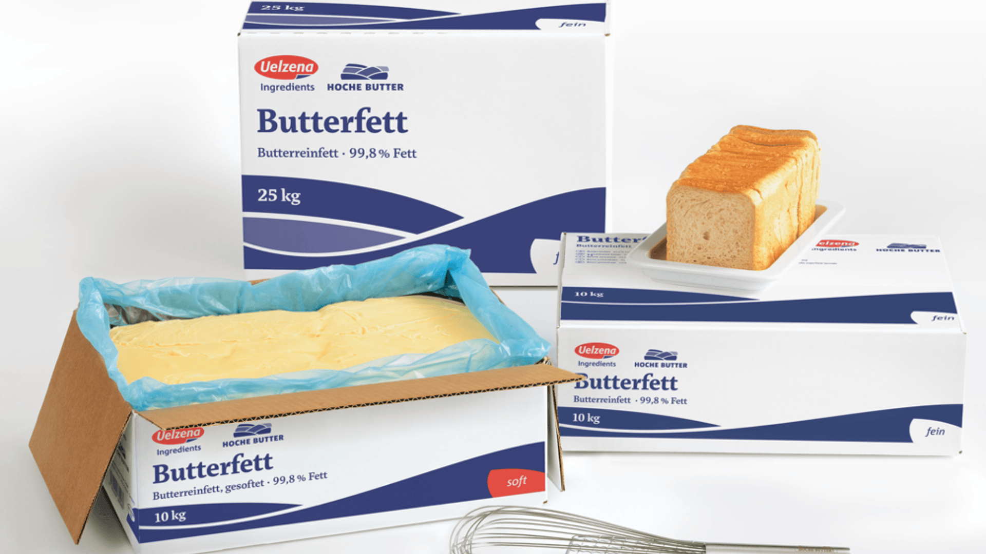 Drei Schachteln mit Uelzena Butterfett, eine davon geöffnet, mit gelber Butter darin. Auf einer Schachtel liegt ein Laib Brot. Davor liegt ein Schneebesen aus Draht. Alle Verpackungen sind weiß und blau.