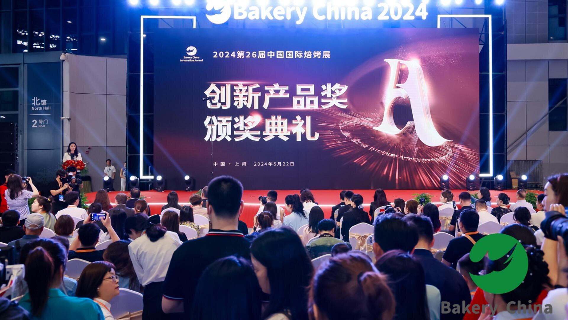 A large crowd attends the 2024 Bakery China Innovative Products Awards ceremony on a stage with bright lights, a big “A” graphic, and event branding in both Chinese and English.
