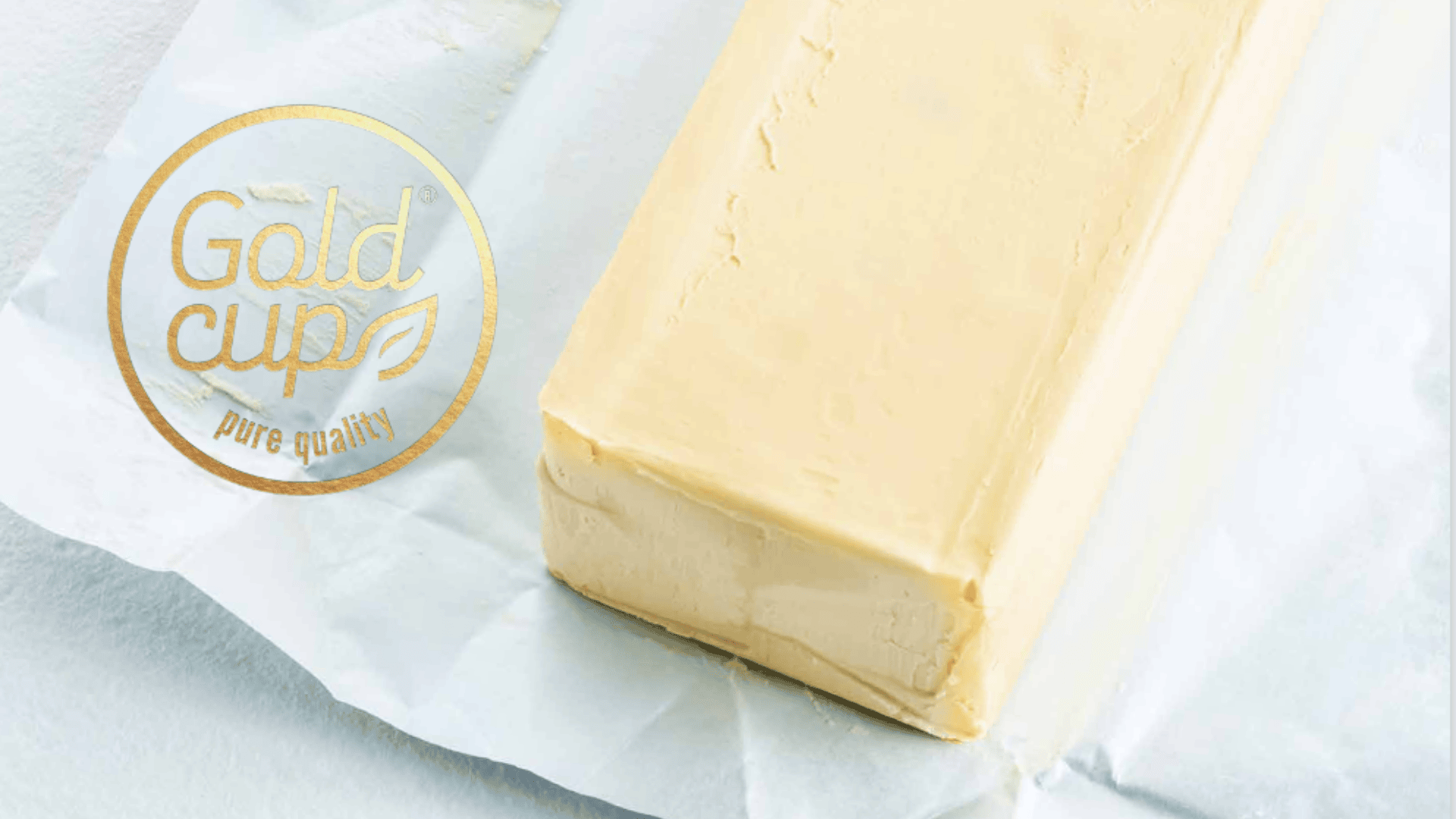 Ein Butterblock liegt auf weißem Pergamentpapier. Das Gold Cup Pure Quality-Logo ist in der linken Ecke des Bildes überlagert.