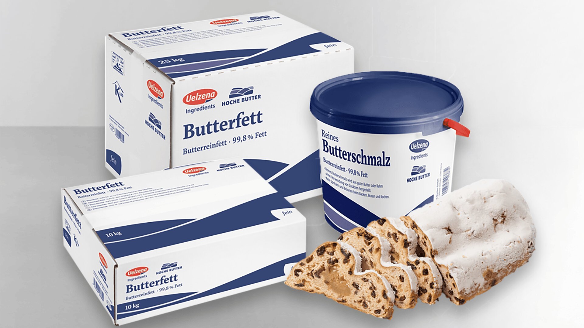 Zwei große Kisten und eine blaue Wanne mit der Aufschrift Butterfett und Butterschmalz sind mit Stollenscheiben, einem traditionellen deutschen Früchtebrot mit Puderzucker, im Vordergrund ausgestellt.