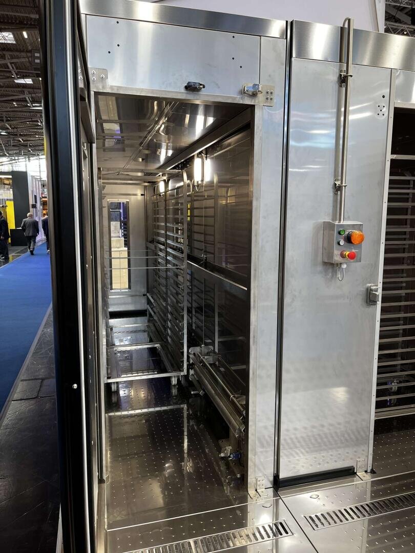 A large industrial stainless steel oven with open compartments and control buttons on the side, located in a well-lit exhibition hall.