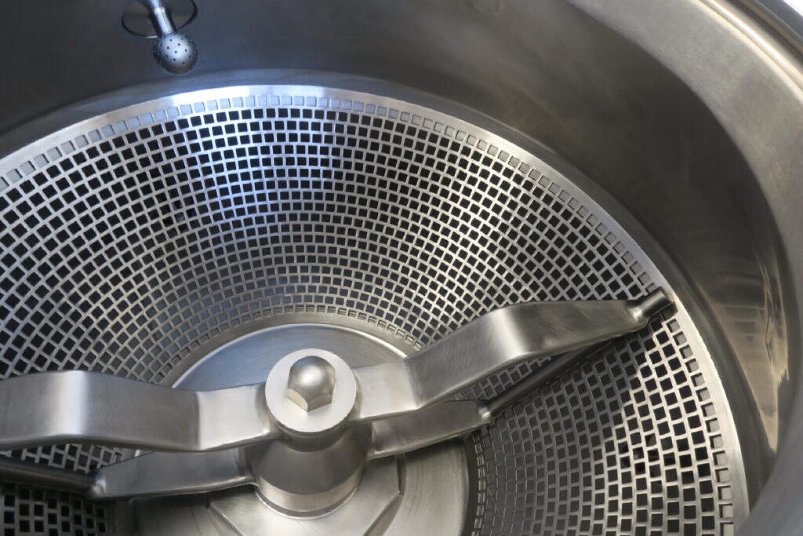 Close-up of the interior of an industrial stainless steel mixing or processing machine with a sieve drum and large rotating mixing blades.