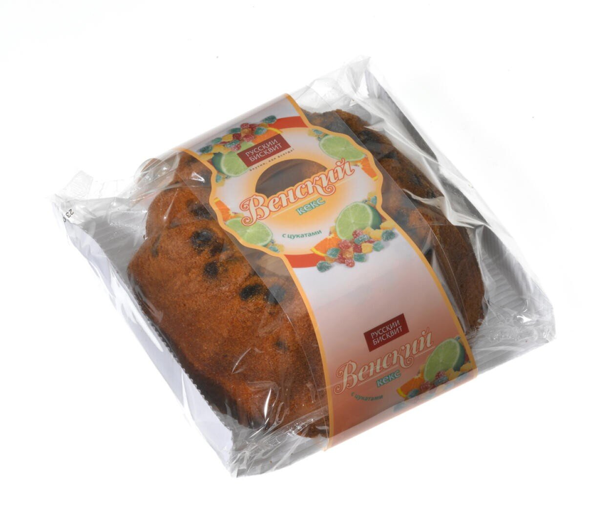 A packaged loaf of fruit cake in a clear plastic wrap with a colorful label featuring illustrations of fruit and Russian text. The cake appears golden brown with visible pieces of dried fruit.