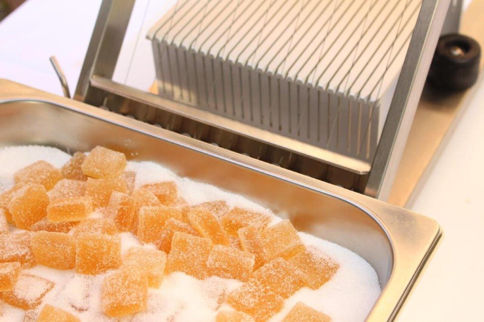 A metal tray filled with sugar-coated yellow jelly cubes sits in front of a slicing machine with evenly spaced wires.