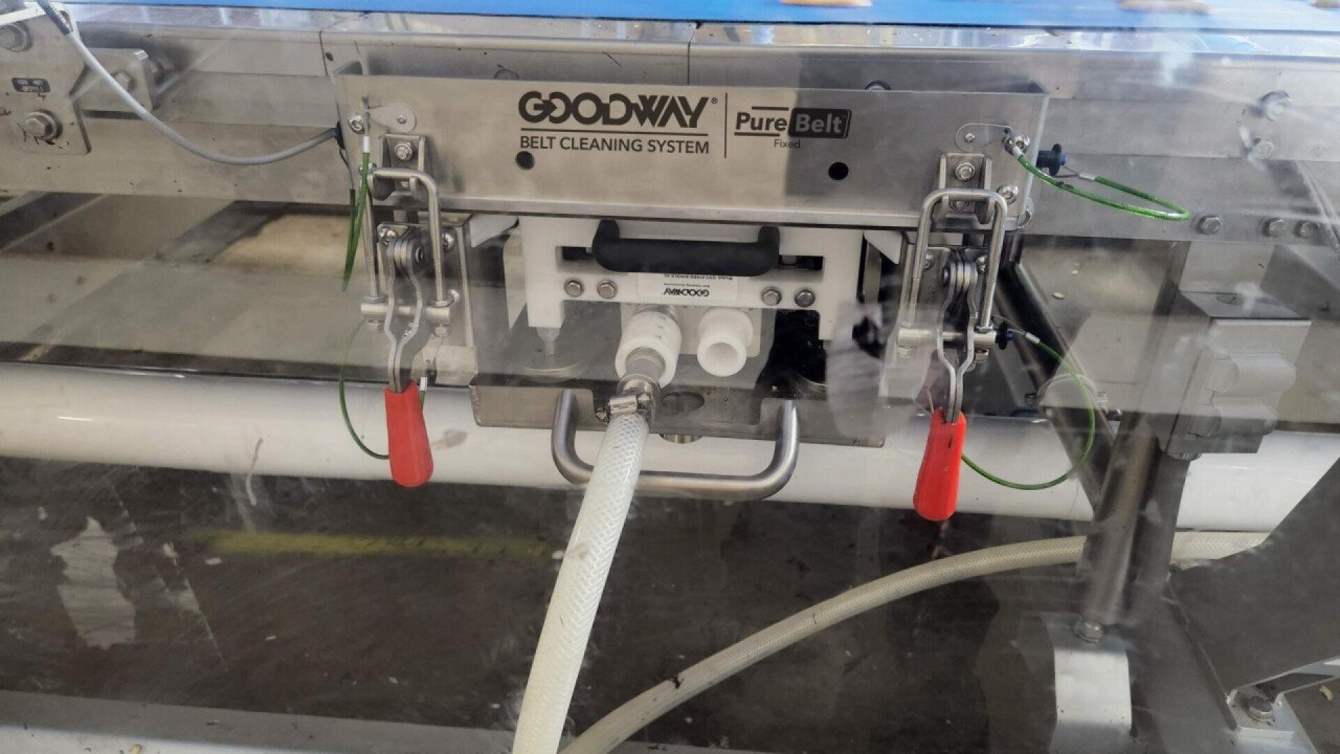 Ein Goodway PureBelt Gurtreinigungssystem mit angebrachten Schläuchen und Metallklammern, montiert an einer Industrieanlage zur automatischen Reinigung von Förderbändern.