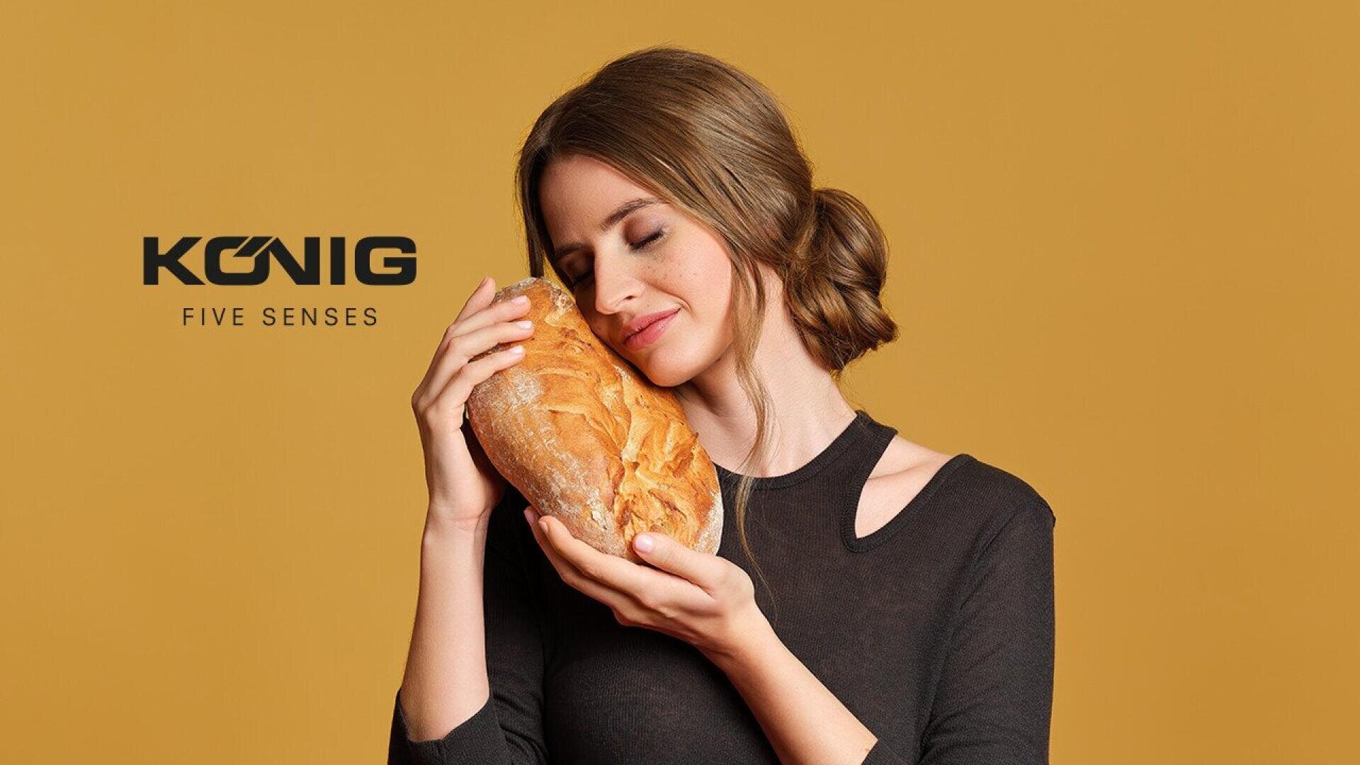 A woman with brown hair, wearing a black top, gently holds and smells a loaf of bread with a content expression. The background is solid yellow, with the text “König Five Senses” on the left.