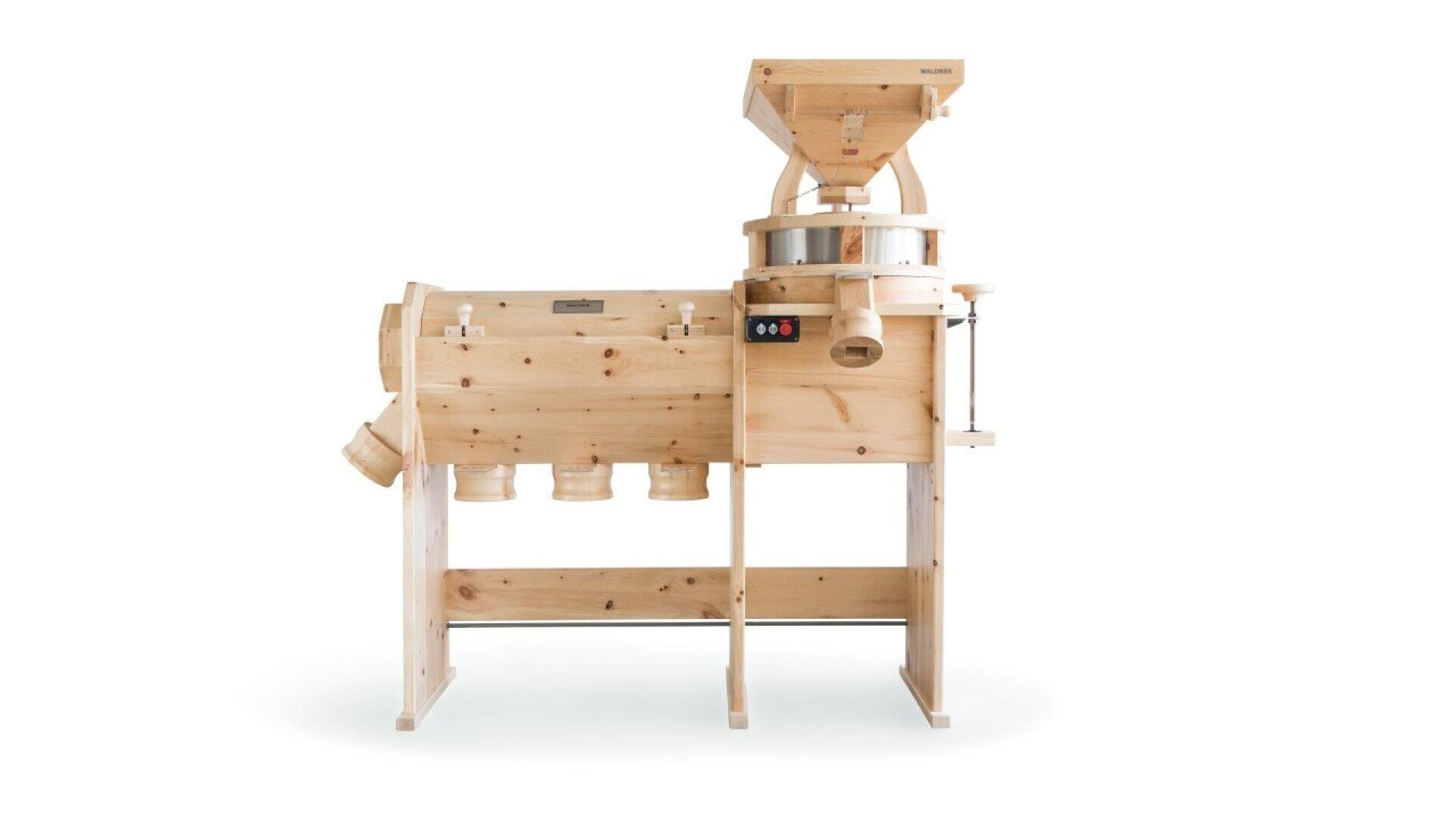 A large, wooden grain mill with multiple collection bins and a hopper on top, designed for grinding grains into flour, is shown against a plain white background.