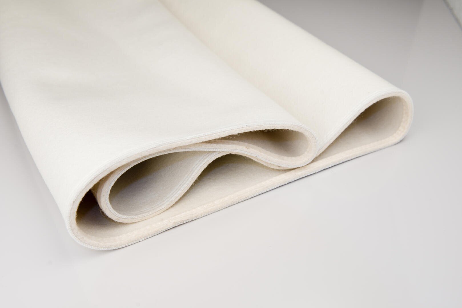 A close-up of a folded piece of white felt fabric on a smooth, light-colored surface. The fabric has a soft texture and clean edges.