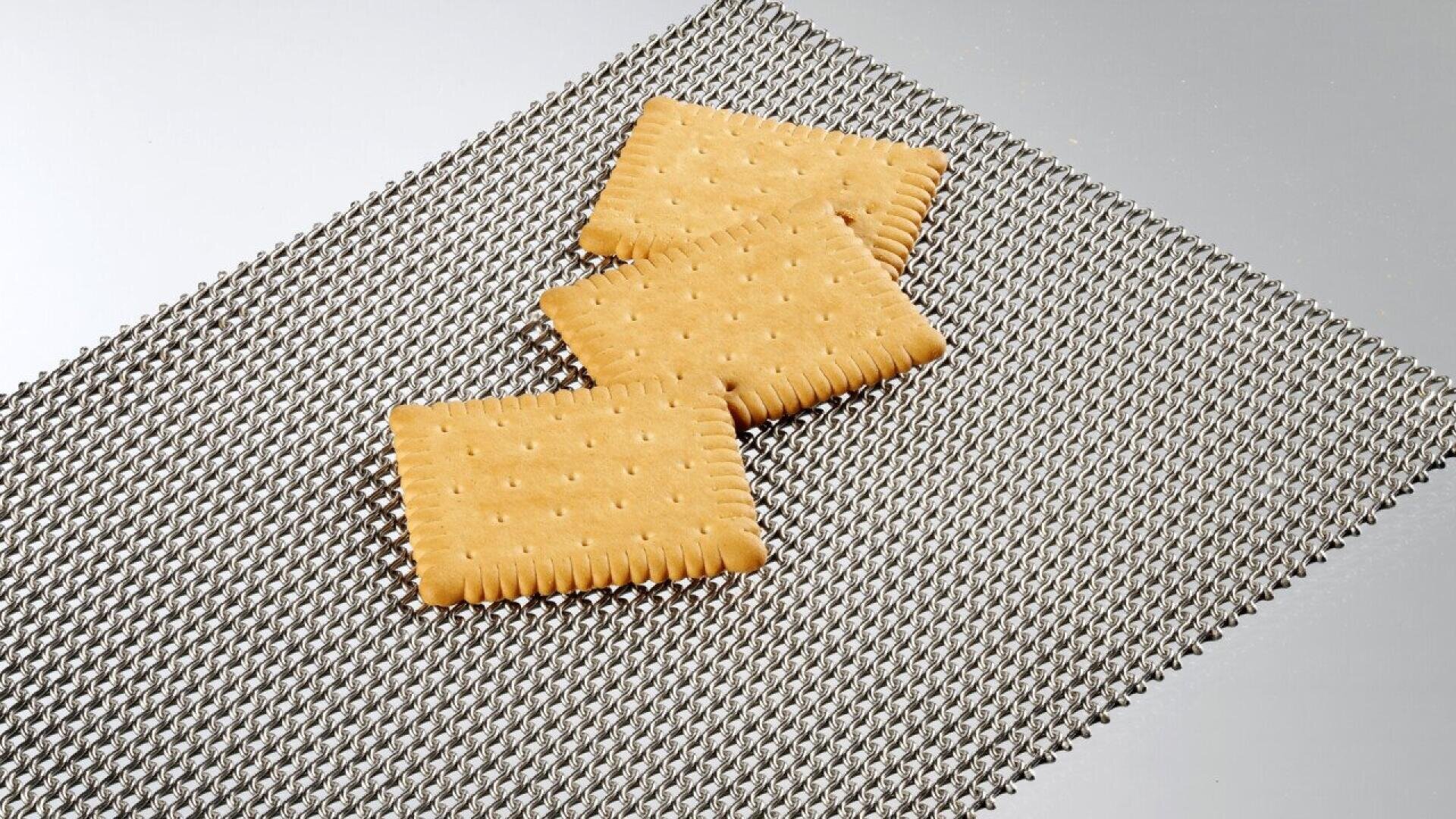 Three rectangular, golden crackers with scalloped edges are arranged on a textured, woven metallic mat against a plain background.