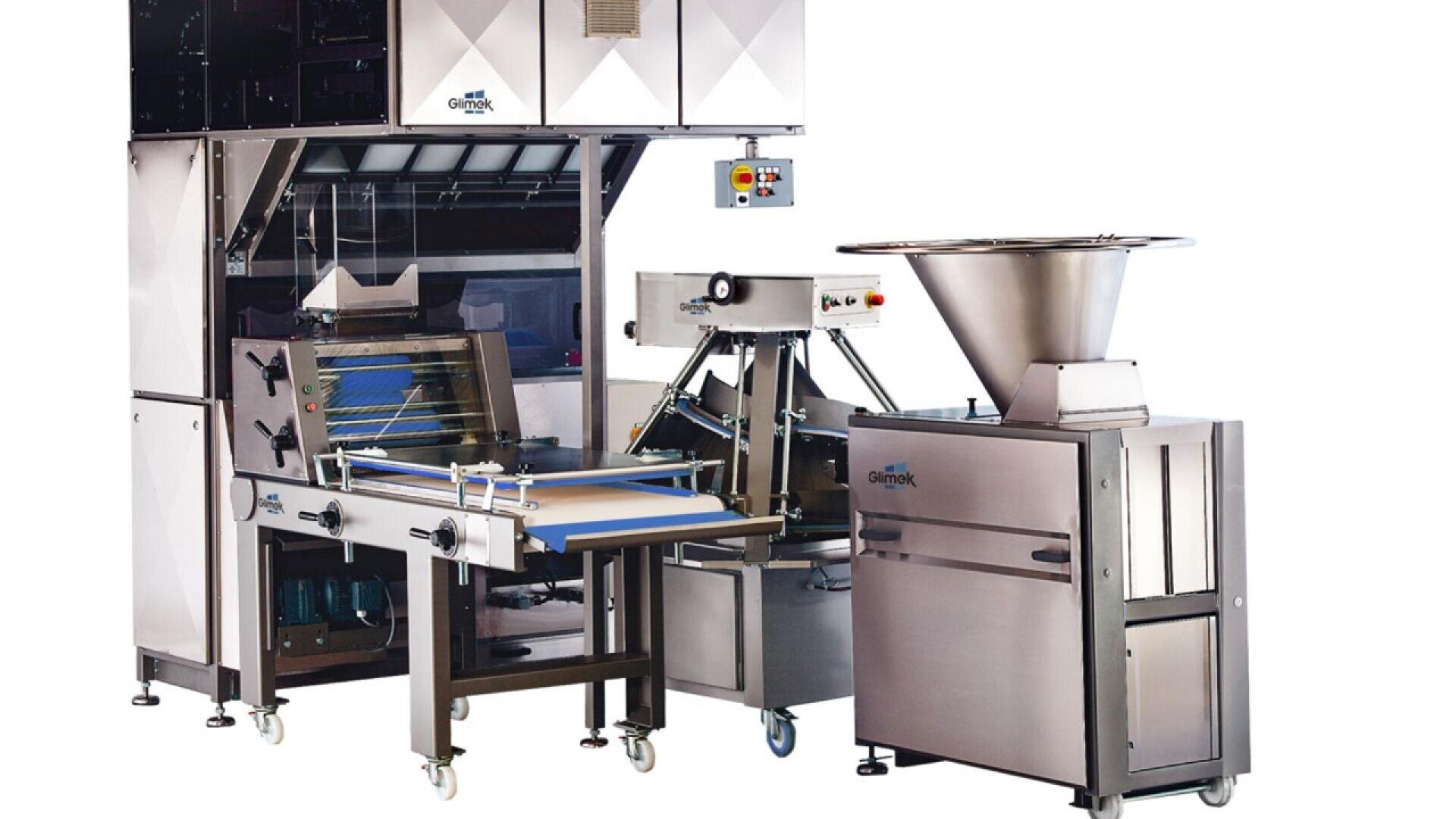 A large, stainless steel industrial food processing machine with conveyor belts, control panels, and a funnel-shaped hopper, set on wheels against a plain white background.
