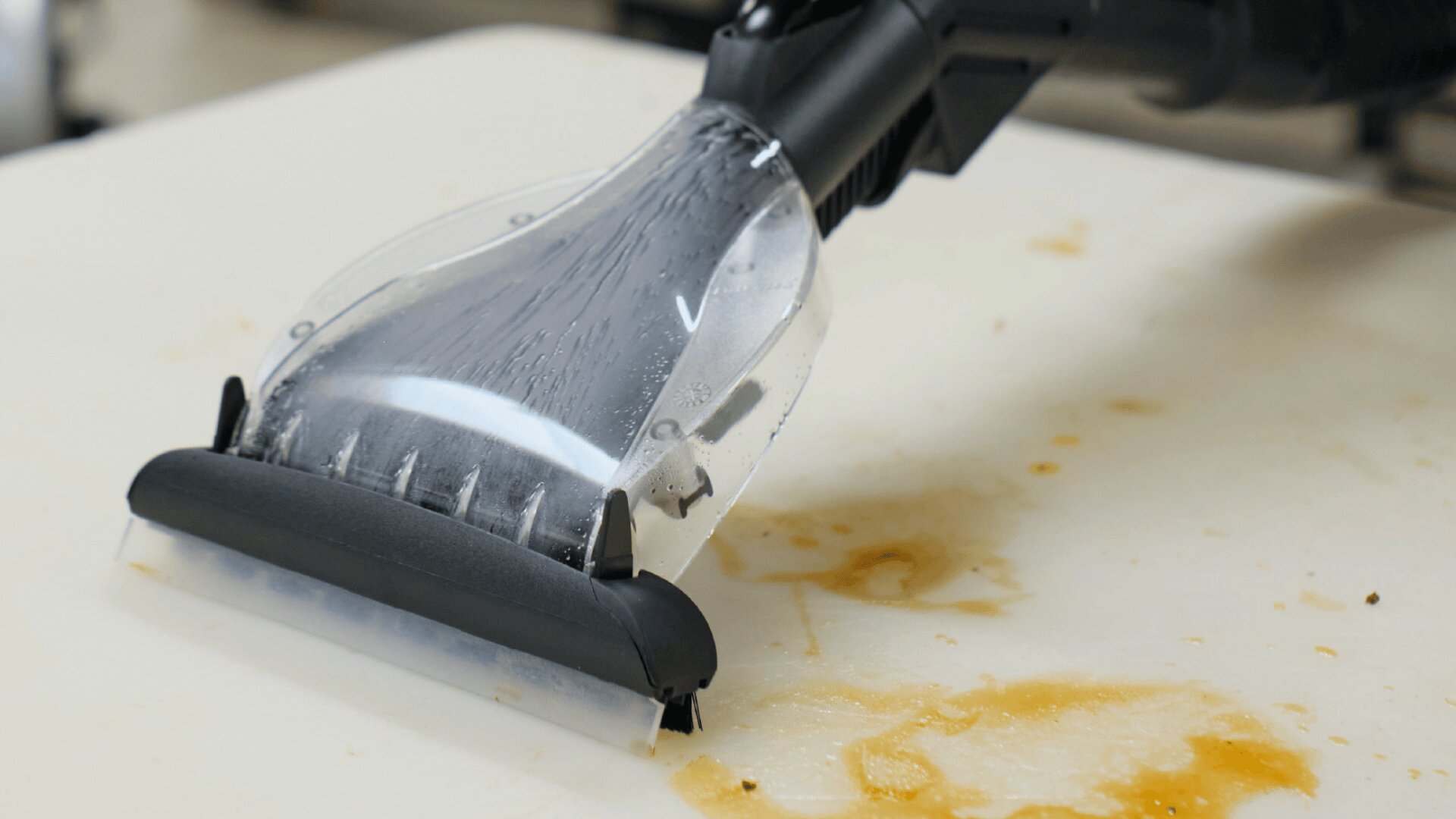 Eine Nahaufnahme einer Teppichreinigungsmaschine, die braune Flecken von einer weißen Oberfläche entfernt, zeigt den Reinigungsprozess in Aktion.