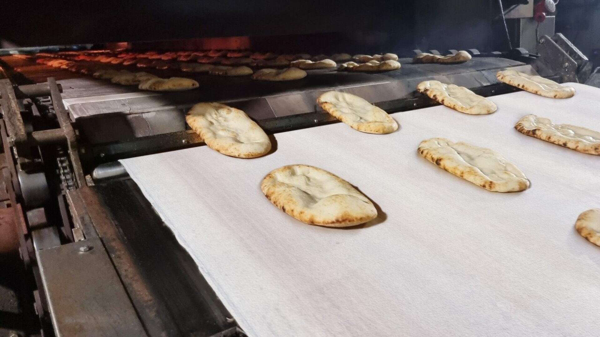 Reihen von Fladenbroten bewegen sich auf einem Förderband in einem Industrieofen und werden in einer gewerblichen Bäckerei gebacken.