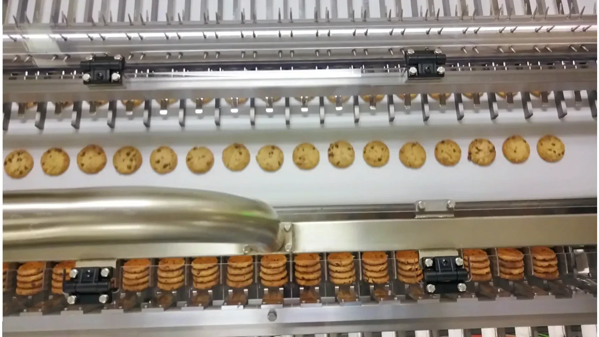 Reihen von Schokoladenkeksen laufen in einer Lebensmittelverarbeitungsmaschine über ein Förderband, wobei eine Reihe zum Verpacken positioniert ist und eine andere Reihe darüber sortiert wird.