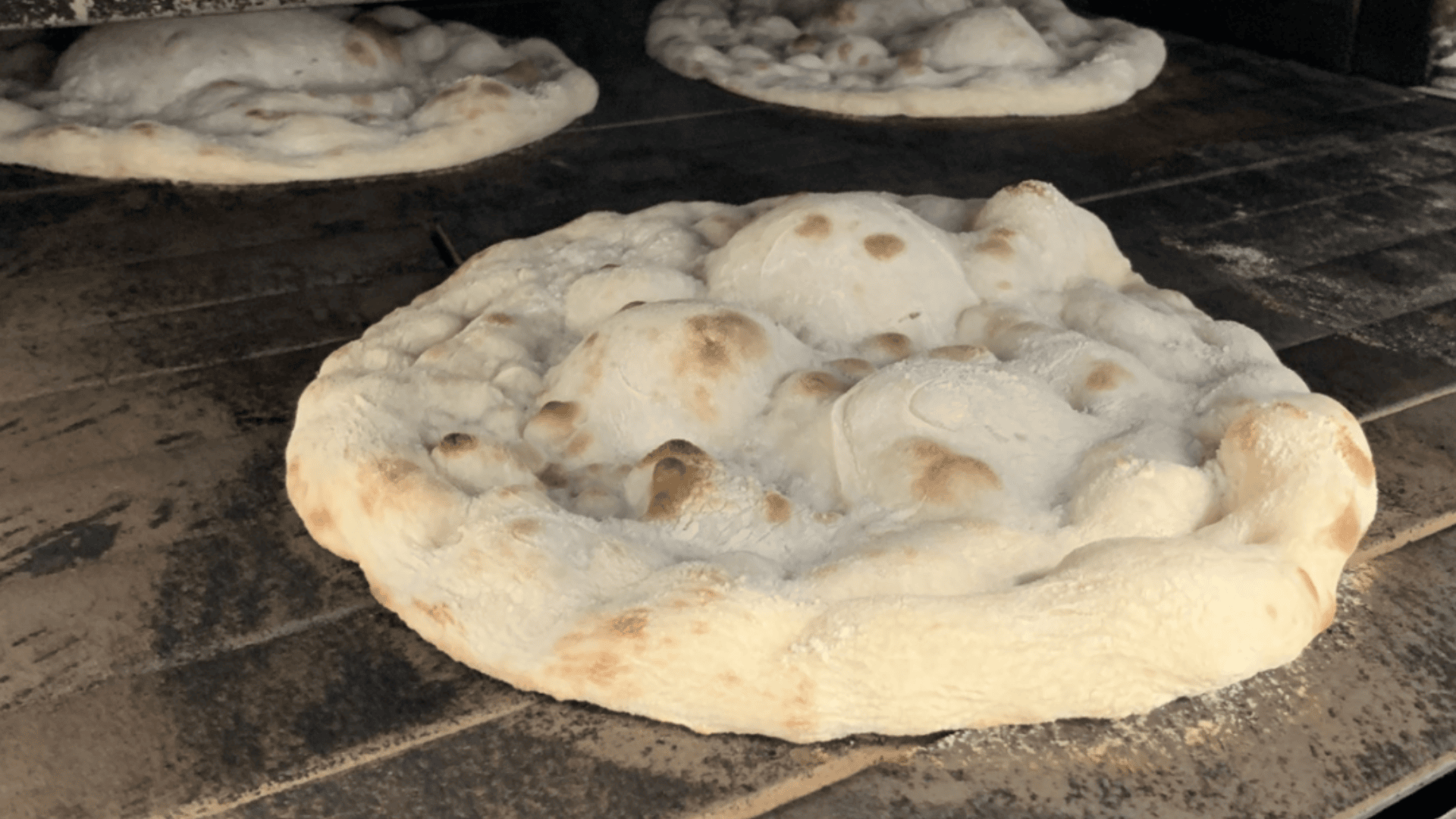 Drei Stücke Pizzateig mit großen Blasen und goldenen Flecken backen direkt auf dem Steinboden eines Pizzaofens.