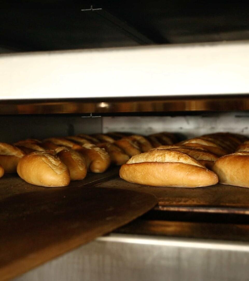In einem großen Industrieofen werden auf Metallblechen reihenweise goldbraune Brötchen gebacken, deren knusprige Kruste durch das warme Licht hervorgehoben wird.