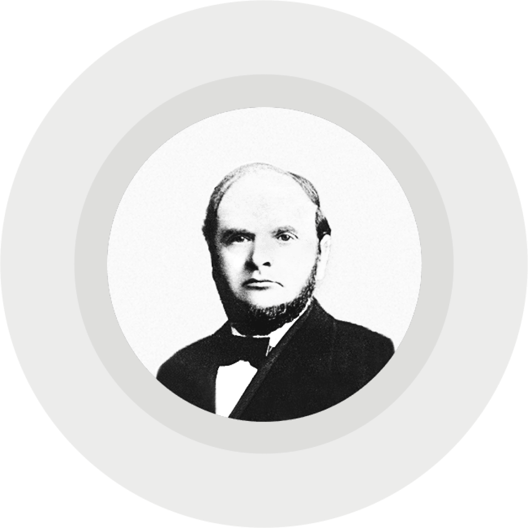 Black and white portrait of a man with short hair, sideburns and a beard. He is wearing a suit with a bow tie in front of a plain light gray background in a round frame.