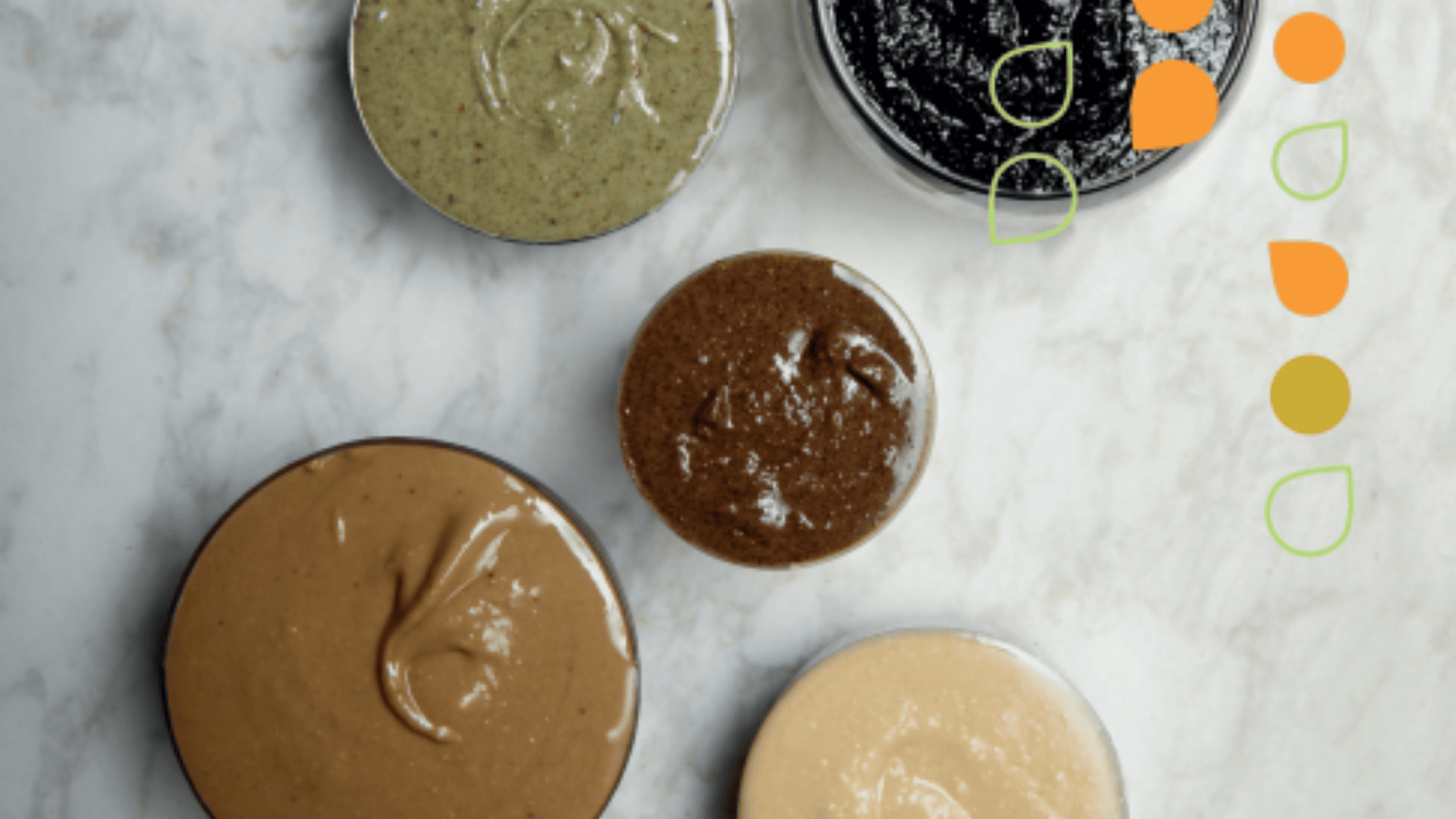 Five bowls of various nut and seed butters are arranged on a white marble surface, with colorful abstract shapes decorating the right side of the image.