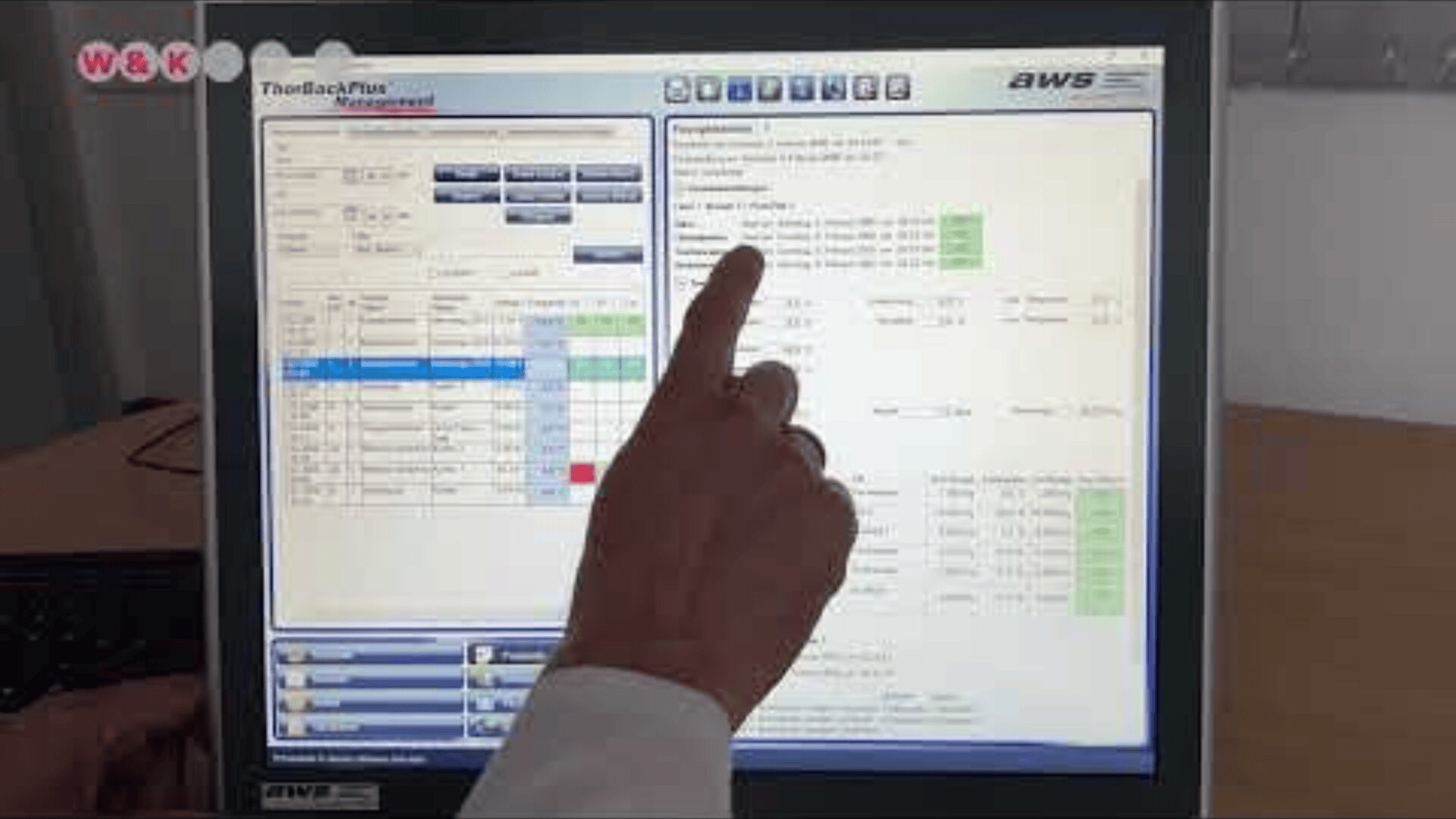Die Hand einer Person zeigt auf einen Computermonitor, der eine Softwareoberfläche mit Tabellen, Diagrammen und hervorgehobenen Datenfeldern anzeigt. Der Bildschirm zeigt verschiedene Menüs, Registerkarten und Informationen in einer professionellen Umgebung.