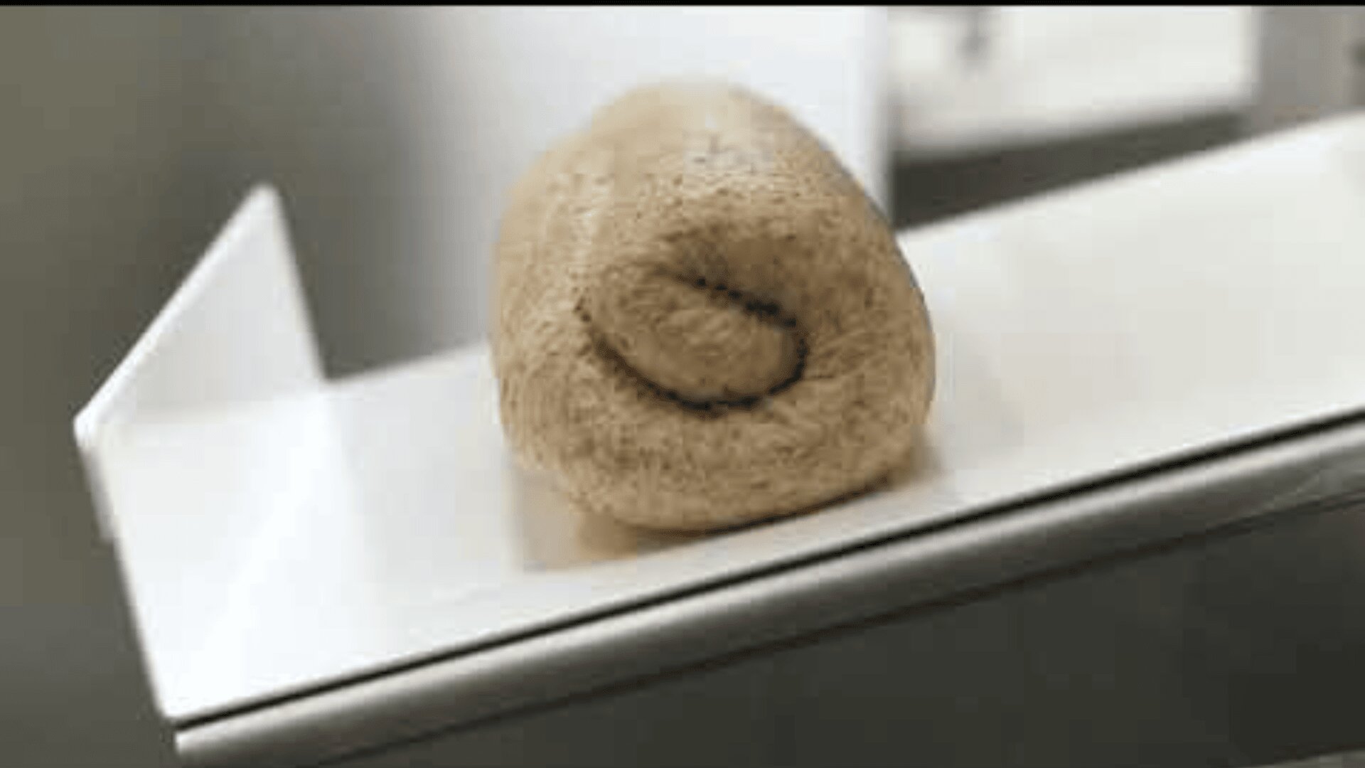 Nahaufnahme eines ausgerollten Teigstücks, das auf einer weißen Fläche liegt, möglicherweise zum Backen vorbereitet. Der Hintergrund ist unscharf und lenkt die Aufmerksamkeit auf die Textur des Teigs.