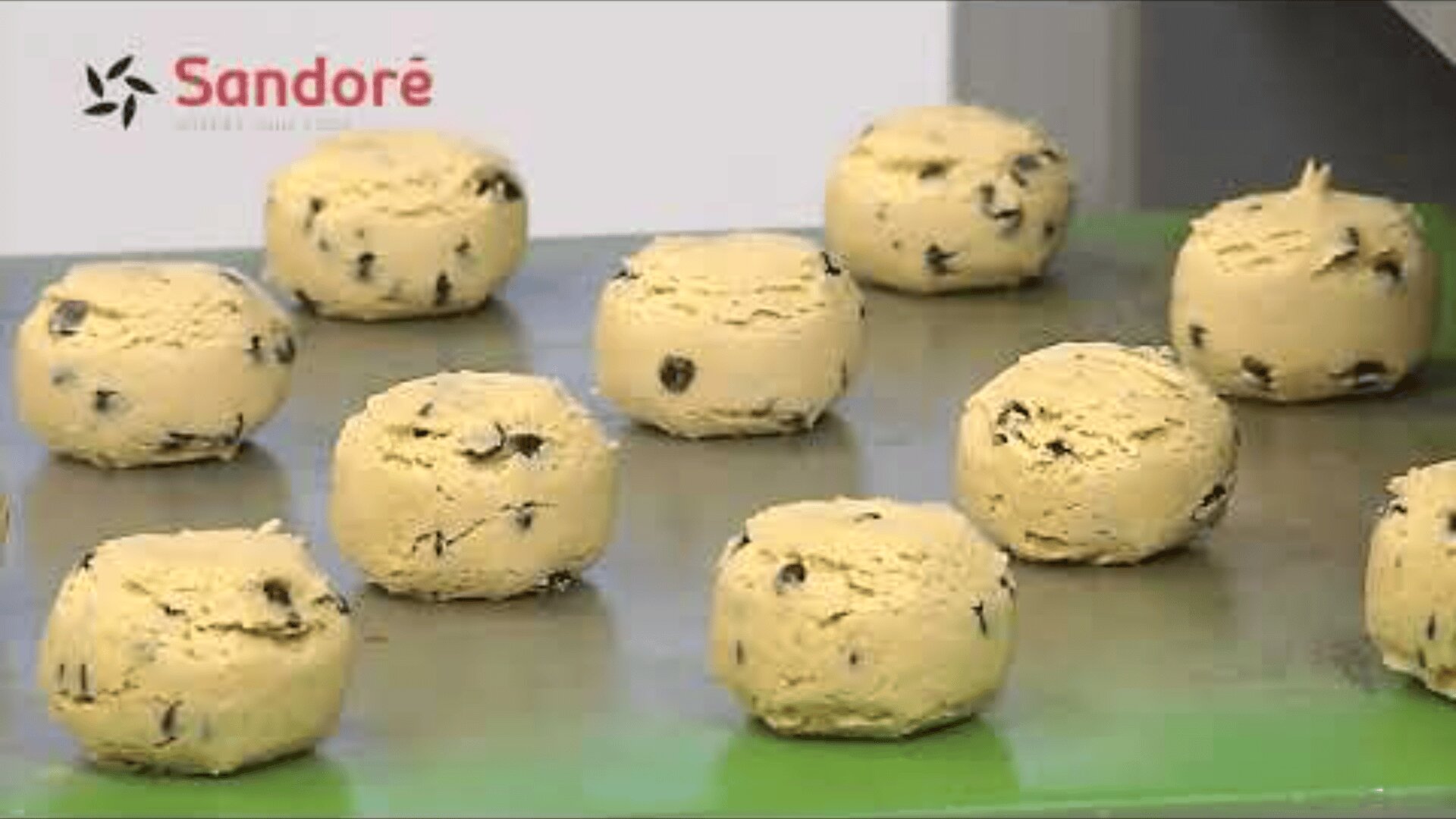 Balls of chocolate chip cookie dough sit on a metal surface, ready to be baked. The Sandoré logo is visible in the top left corner.