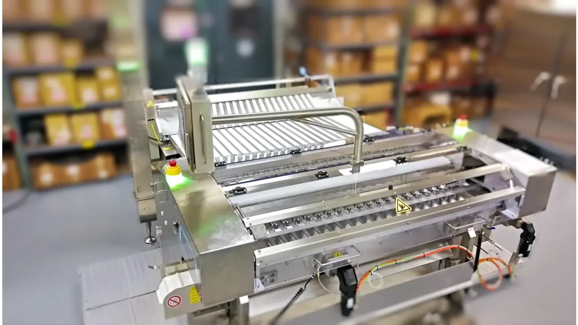 Automatisierte Verpackungsmaschine mit Metallrollen und Fördersystem in einem Lager, umgeben von Regalen mit Kartons im Hintergrund.