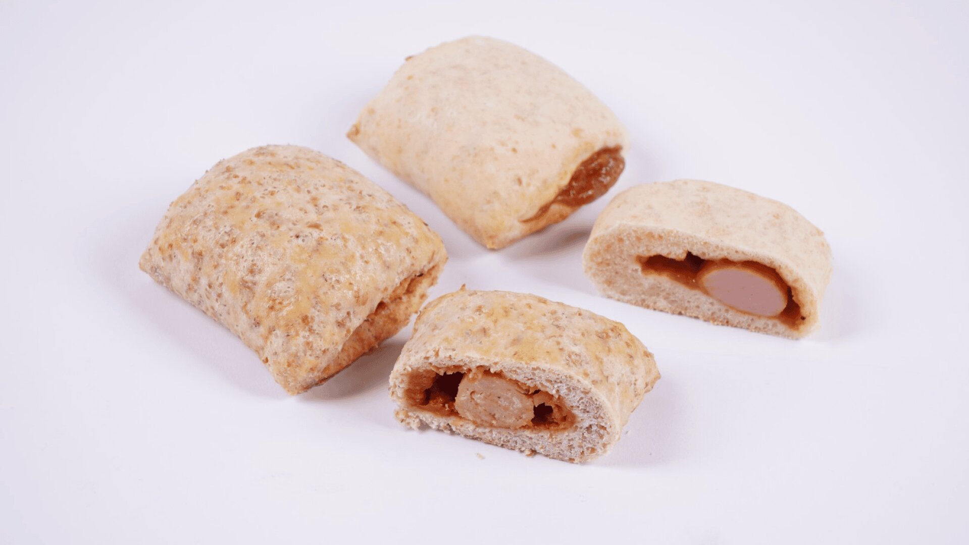 Vier Vollkornbrottaschen mit einer Wurstfüllung auf weißem Hintergrund, eine Tasche ist aufgeschnitten und gibt den Blick auf die Wurst und die Soße frei.