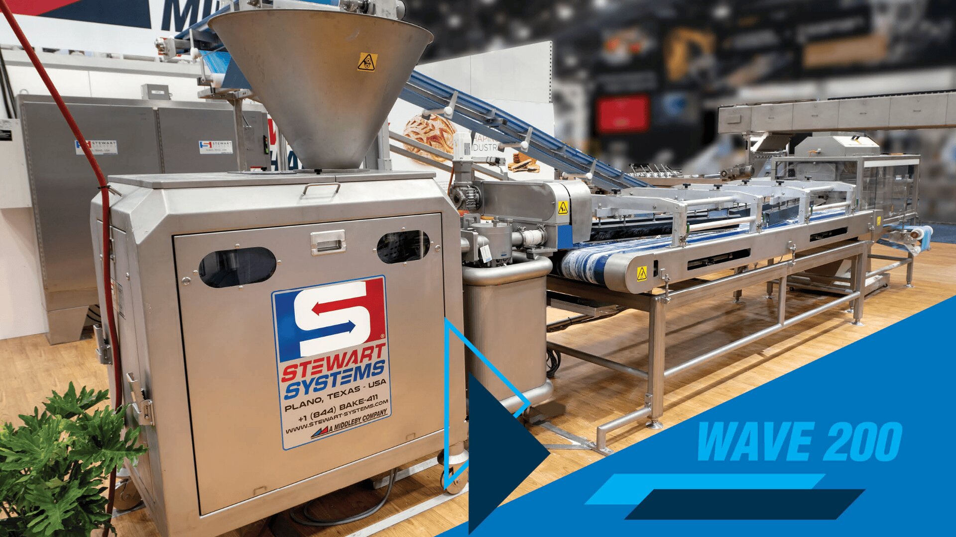 Industrial bread processing machine by Stewart Systems with conveyor belts and large metal components, displayed indoors at an exhibition. Blue graphic text reads “WAVE 200” in the lower right corner.