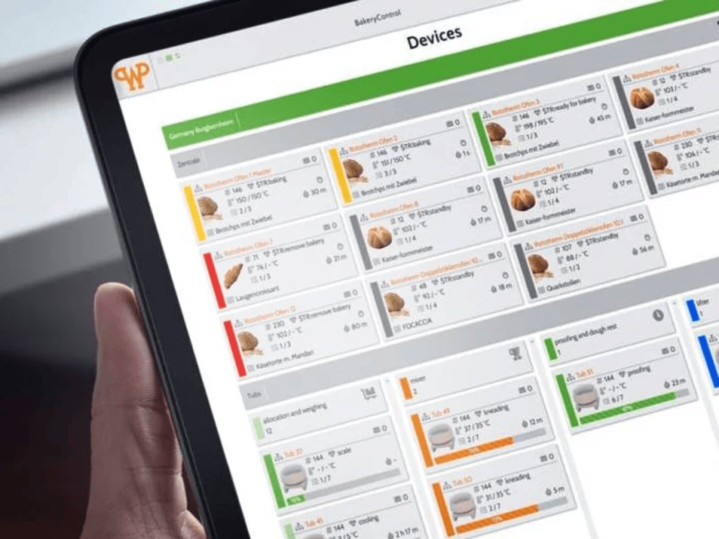 A person holds a tablet displaying a dashboard titled Devices, showing various device status cards organized in rows with colored bars, icons, and technical details on the screen.