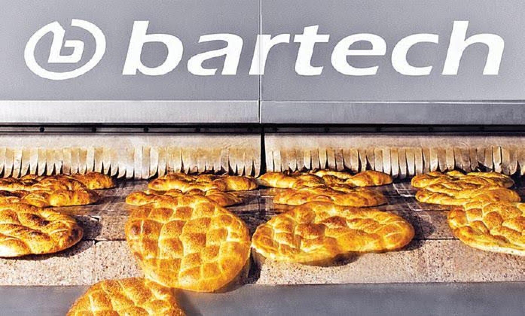 In einer Bäckerei oder einem industriellen Backbetrieb laufen frisch gebackene Brotlaibe über ein Förderband unter dem großen bartech-Firmenlogo.