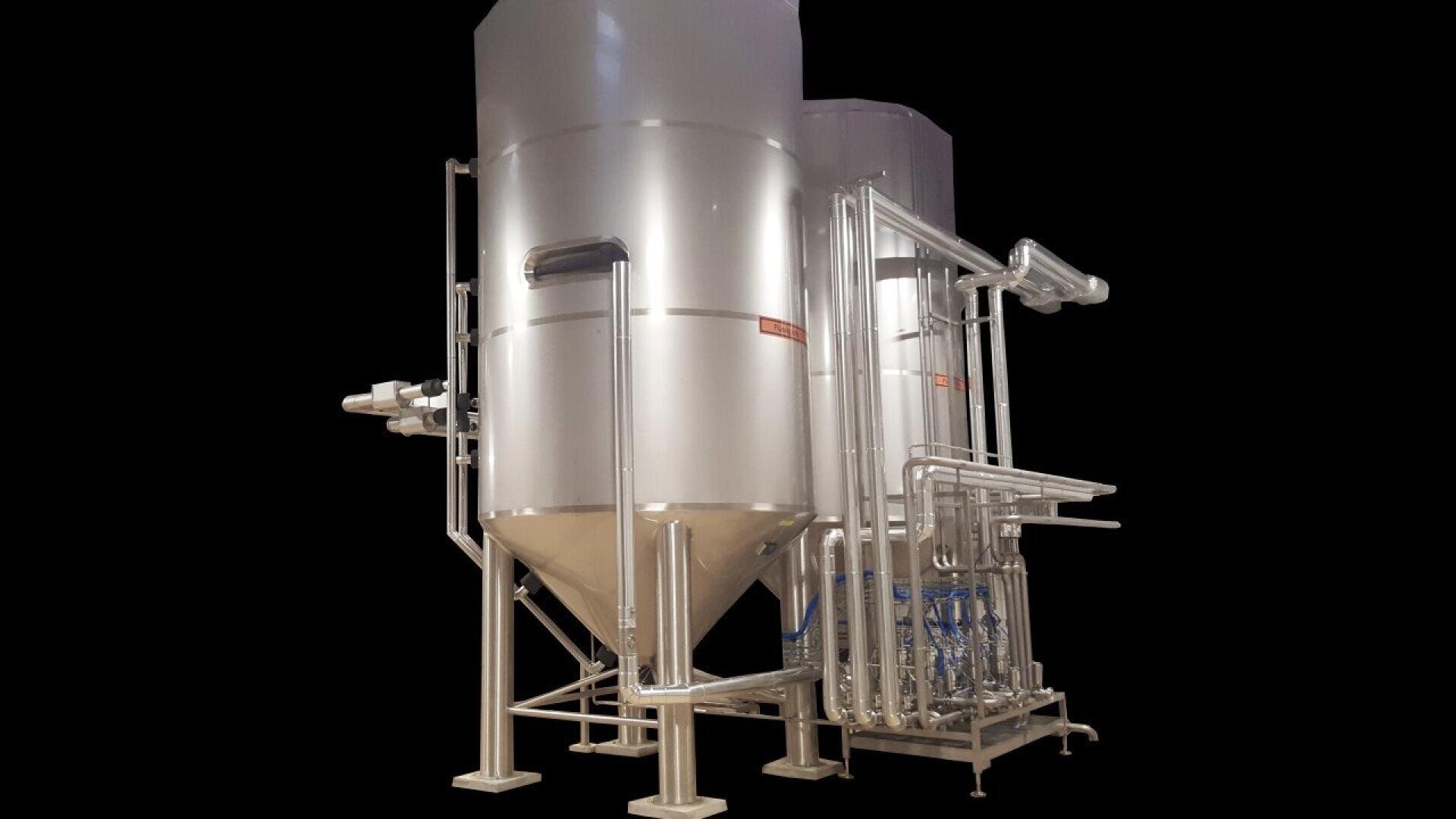 Large industrial stainless steel tanks with conical bases, connected by a network of pipes and valves, used for processing or storing liquids, set against a plain black background.