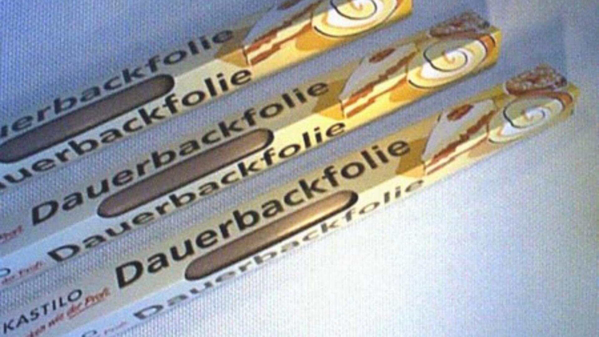 Three packages of Dauerbackfolie, a reusable baking foil, are arranged diagonally on a light surface. The packaging is mostly white and yellow with text and images of baked goods.