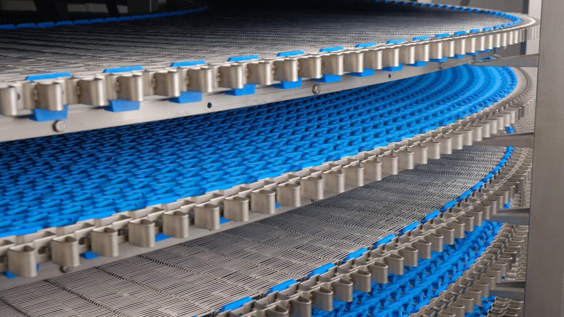 Nahaufnahme eines mehrstufigen Spiralfördersystems mit Metall- und blauen Kunststoffbändern, die sich um die Struktur schlängeln und typischerweise in der industriellen Lebensmittelverarbeitung oder -herstellung eingesetzt werden.