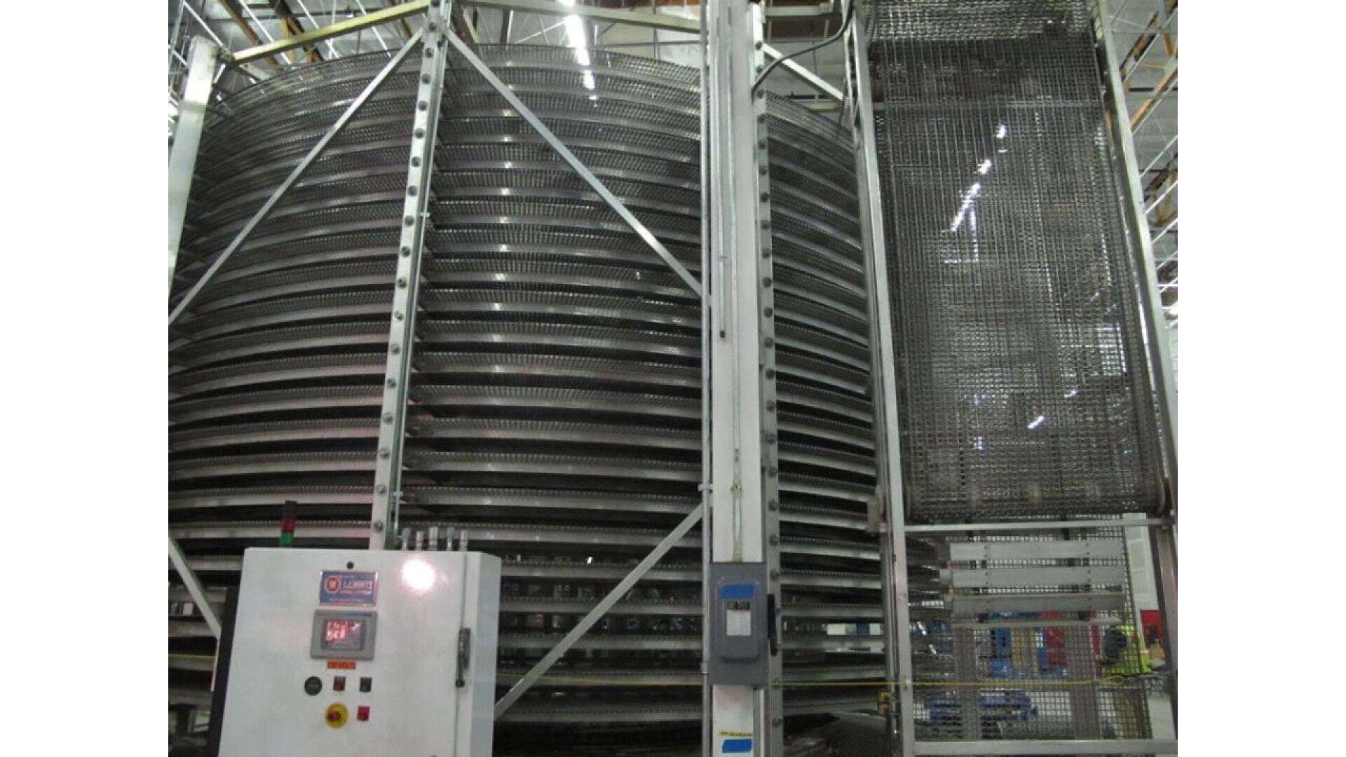 Industrielles Spiralfördersystem mit mehreren rotierenden Metallebenen, die von einem Metallrahmen umgeben sind. Auf der linken Seite der Maschine befindet sich ein Bedienfeld mit Tasten und einem Display.