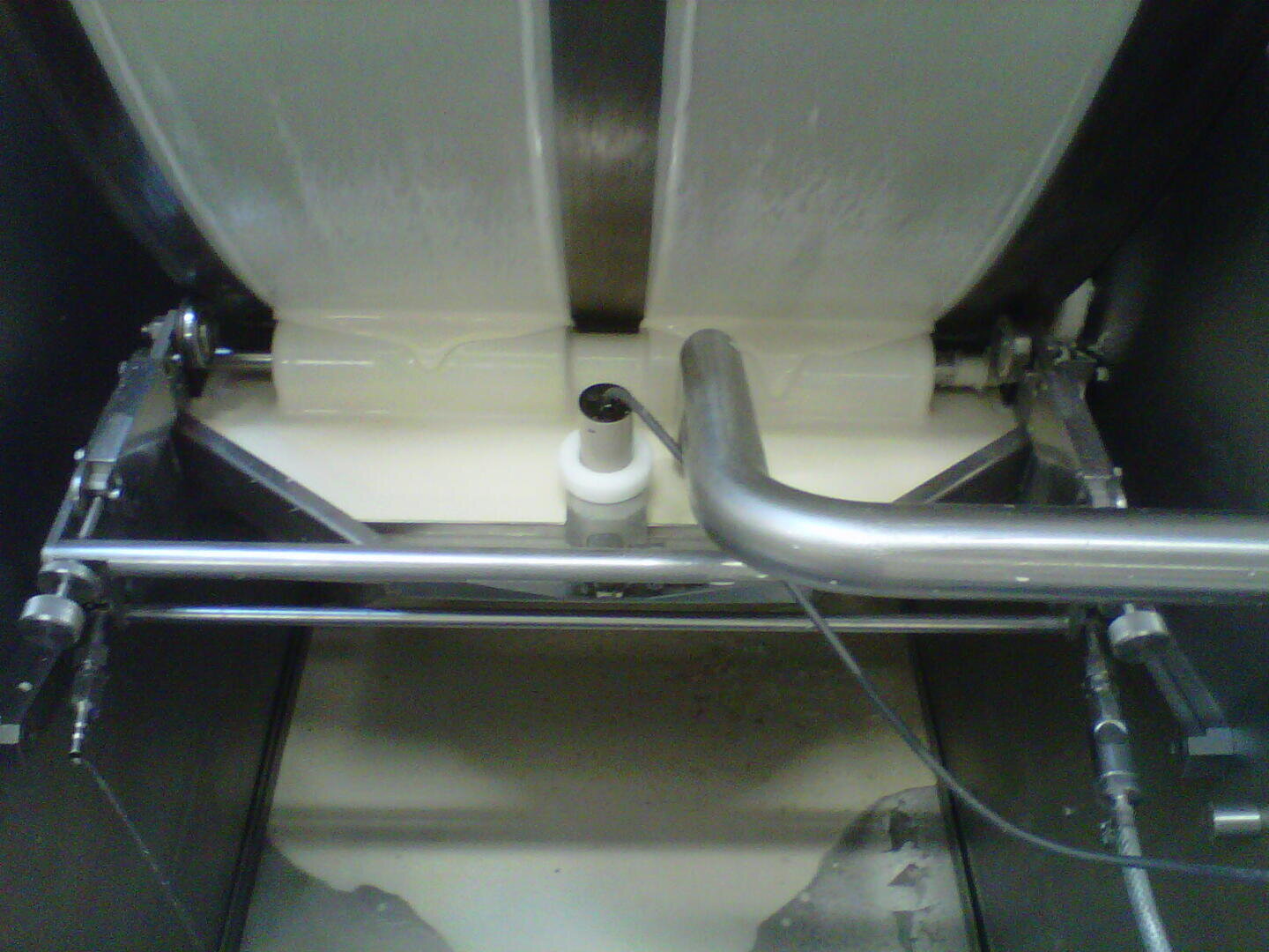 Close-up of an industrial butter churn in operation, with metal paddles mixing and processing a creamy white substance inside a stainless steel container.