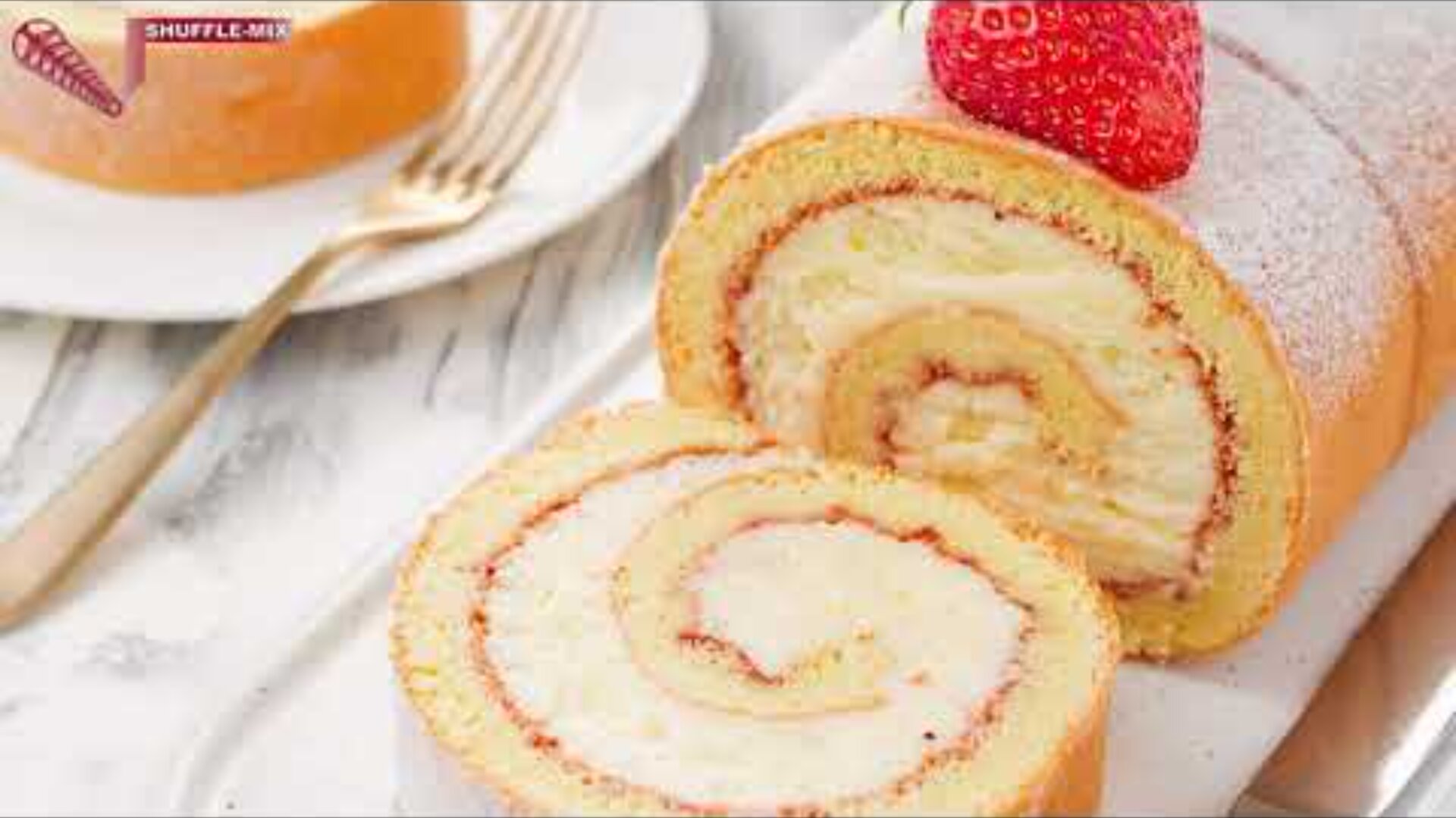 Nahaufnahme eines in Scheiben geschnittenen Schweizer Rollkuchens mit einer cremigen Strudelfüllung, gekrönt mit einer frischen Erdbeere, auf einer weißen Marmorfläche neben einer Gabel und einem Teller.