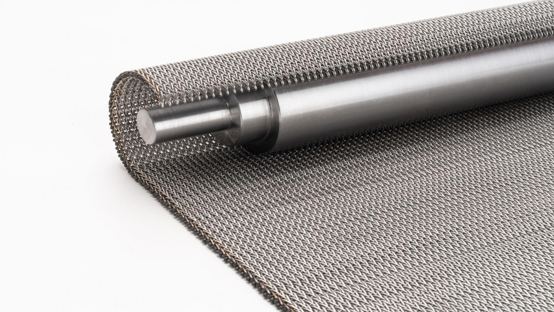 A close-up of a metal mesh fabric partially rolled around a metallic cylindrical rod, set on a white background.
