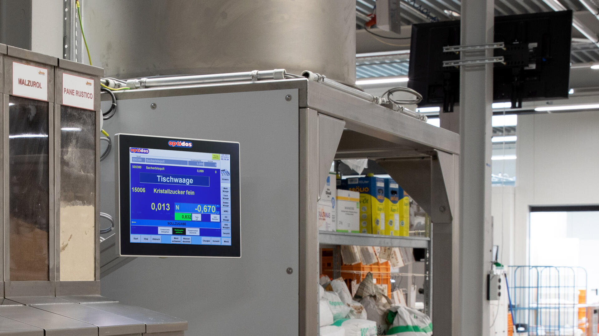 Eine Industriewaage zeigt die Messwerte auf einem digitalen Bildschirm neben den Metallregalen an, die mit verschiedenen verpackten Waren in einer Fabrik oder einem Lager gefüllt sind.