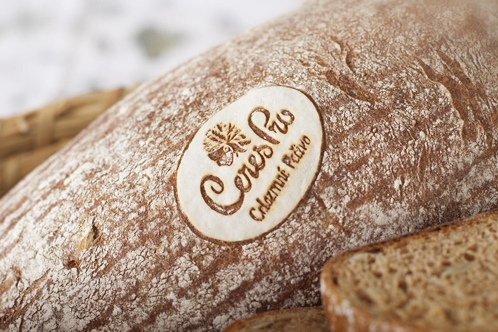 Nahaufnahme eines rustikalen Brotlaibs mit einem runden weißen Etikett, auf dem das Logo und der Name "CeresBio" sowie der Schriftzug "Celamik Extra" eingeprägt sind. Im Vordergrund sind teilweise Brotscheiben zu sehen.